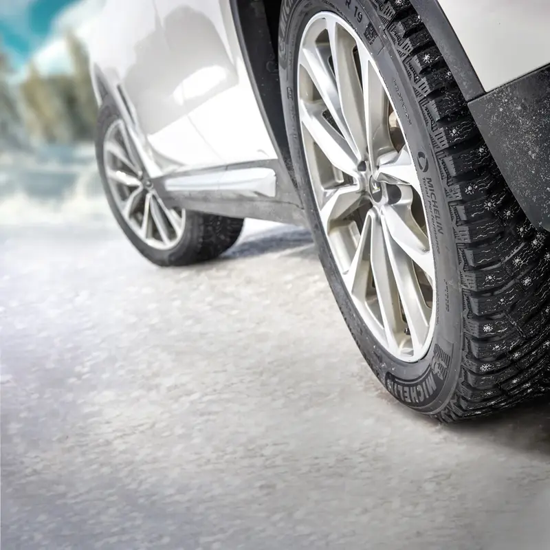 Close up picture of Winter Tires on a silver vehicle on a snowy street.